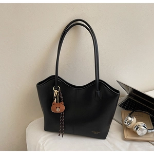 Detail of matte black tote bag with wavy rim, brown bear charm, and gold logo text