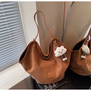 Detail of brown suede hobo tote bag featuring a leather logo tag and cloud plush charm