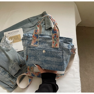 Detail of denim tote bag with colorful floral embroidery straps and silver metal buckle