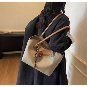 Detail of a minimalist cream faux leather tote bag with brown straps and a bear pendant