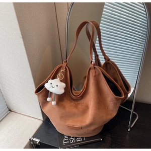 Detail of brown faux suede tote bag with wavy trim, leather logo, and fluffy cloud charm