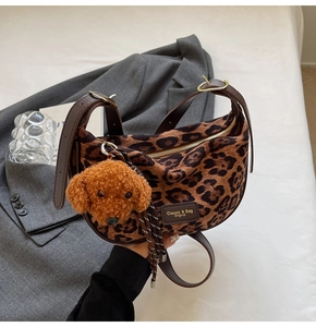 Detail of leopard print hobo bag with leather strap and plush dog charm on white linen