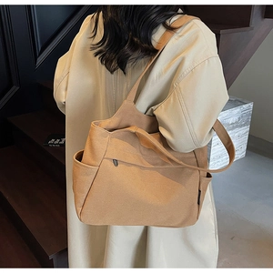 Vista dettagliata di una grande borsa tote in tela caramello portata a spalla da una modella