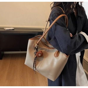 Detail of beige leather tote bag with brown trim and cute plush bear charm accessory
