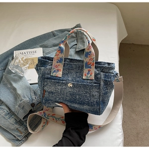 Detail of blue denim tote bag featuring exquisite floral embroidery on handles and strap