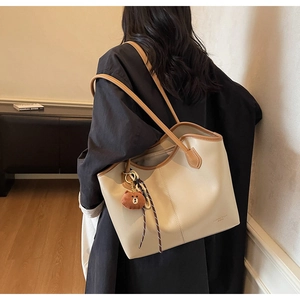 Detail of a large cream tote bag with brown straps and a cute plush bear pendant accessory