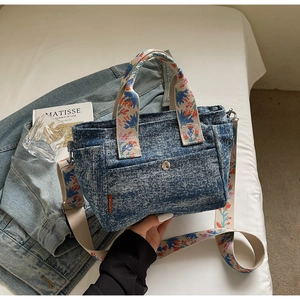 Detail of blue denim tote bag featuring floral pattern strap and magnetic metal closure