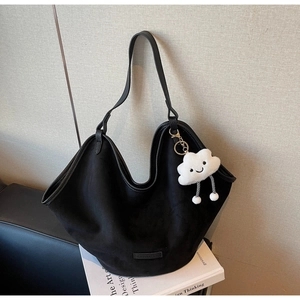 Detail of black faux suede tote bag with leather trim and white cloud plush pendant