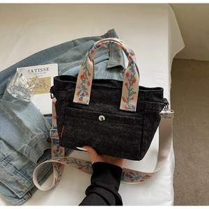 Detail of black denim tote bag featuring embroidered floral straps and magnetic front pocket