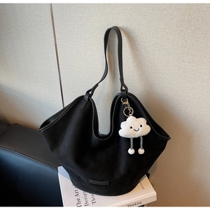 Close-up of large black suede tote bag with white cloud plush charm and brand tag