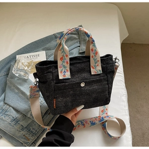 Detailed view of dark denim tote bag featuring floral woven strap and magnetic pocket