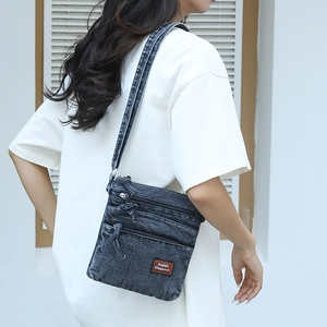 Detail of vintage washed denim crossbody bag with multiple zip pockets and brand leather patch