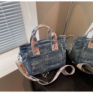 Detailed close-up of blue denim tote bag with colorful floral embroidered handles and strap