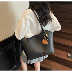 Detail of large black PU leather tote bag with cute bear charm worn on shoulder