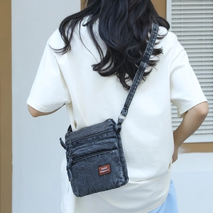 Detail of dark grey washed denim crossbody bag with multi-layer zippers and leather label