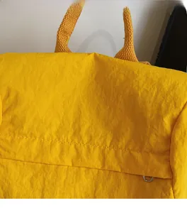 Detalle de una mochila de nailon amarillo con textura arrugada, asa de cinta y anillo D