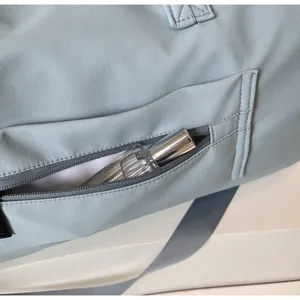 Detail of light blue nylon travel bag showing a side zipper pocket and grid texture