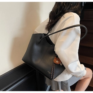 Detail of black faux leather tote bag with thin straps and cute brown bear keychain charm