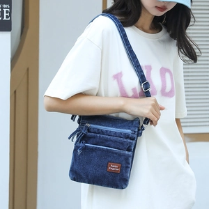 Detailed view of dark blue denim crossbody bag with adjustable strap and leather logo patch