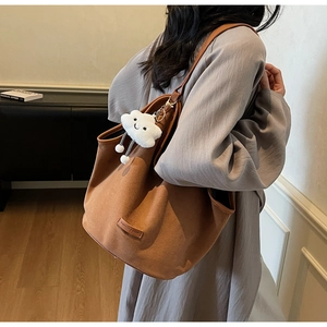 Detail of a large brown suede tote bag featuring a fashion tag and cloud charm accessory