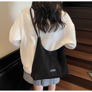 Dettaglio borsa hobo in camoscio nero con tracolla larga e placchetta logo moda