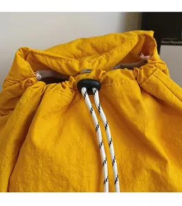 Detalle de mochila de nailon amarillo con cierre de cordón ajustable y tope de plástico