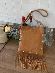 Vintage brown suede crossbody bag with metal rivets and long tassels on white background