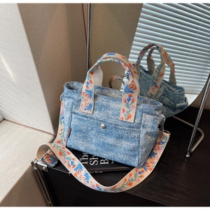 Detail of blue denim tote bag with colorful floral embroidered straps and silver snap pocket