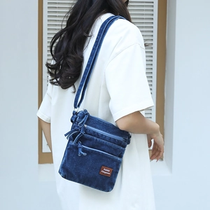 Close-up of a vintage washed denim crossbody bag featuring multi-layer zipper compartments