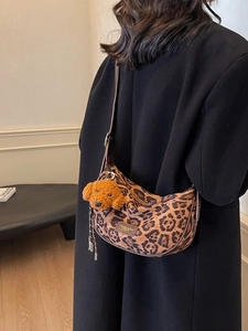 Leopard print hobo shoulder bag with plush dog charm shown on a black winter coat