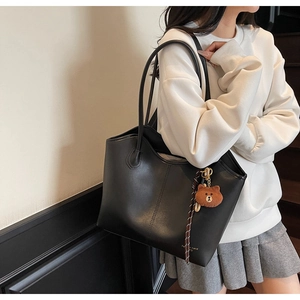 Detail of a large black leather tote bag featuring a cute plush bear charm on a model