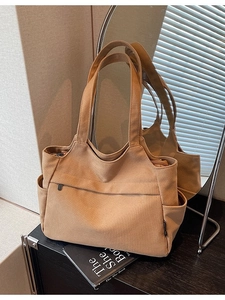 Borsa tote in tela kaki resistente con tasche laterali esposta in una stanza elegante