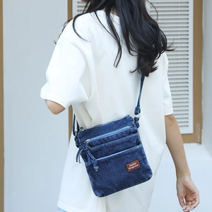 Detail view of retro washed denim crossbody bag featuring multiple zippers and leather logo patch