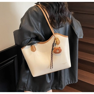 Detail of cream tote bag with brown trim and cute bear pendant on a leather jacket shoulder