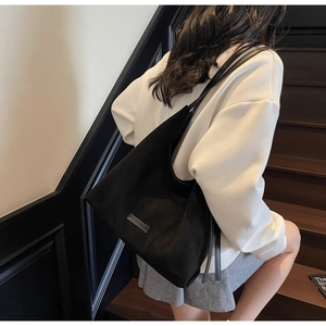 Modella che indossa una borsa a spalla in camoscio nero con tracolla su sfondo di scale sobrie