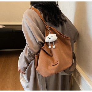 Detail view of large brown tote bag with a white plush cloud charm and fashion label