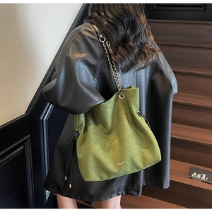 Détail du sac seau en daim vert foncé avec bandoulière chaîne et pompons à cordon