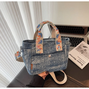 Detail of blue denim tote bag with floral embroidered handles and adjustable shoulder strap