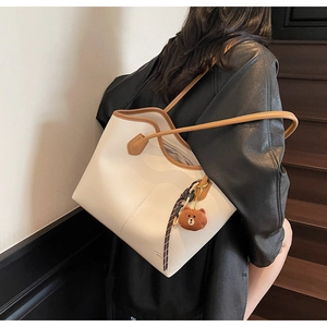 Detail of white tote bag with brown leather trim and cute bear charm worn on shoulder