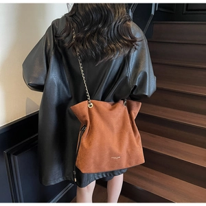 Sac fourre-tout en daim marron avec bandoulière chaîne dorée porté par un mannequin