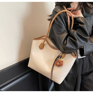 Detail of white tote bag with brown trim and bear charm shown on model's shoulder