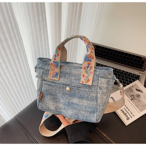 Detail of denim tote bag with colorful floral embroidery handles and shoulder strap
