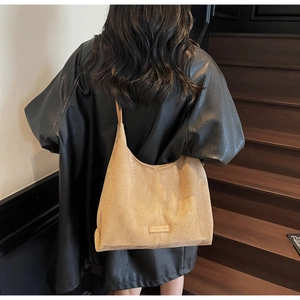 Dettaglio della texture scamosciata color cammello della borsa tote e logo su giacca