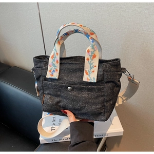 Detail of grey denim tote bag featuring floral embroidery on the handle and strap