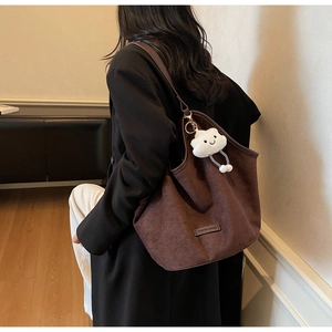 Detailed view of coffee brown tote bag with white cloud plush charm on model shoulder