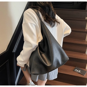 Detailed view of black pebbled leather tote bag worn by a model on wooden stairs