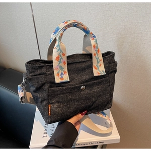 Detail of black denim tote bag with colorful floral embroidery on webbed handles