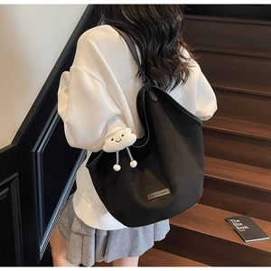 Detail of black suede tote bag with white cloud plush pendant on dark wood stairs