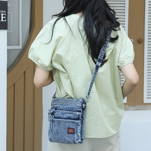 Detail showing vintage washed denim crossbody bag with multiple zipper compartments