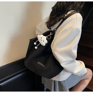 Detail of a large black tote bag with a white fluffy cloud pendant and a leather brand label
